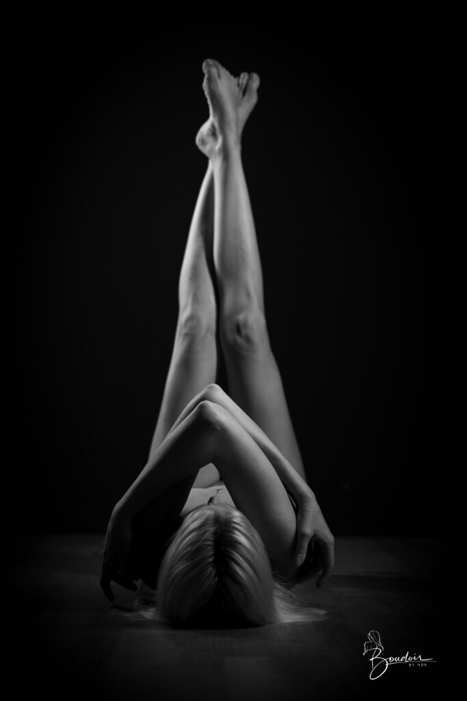 Venisis allongée sur le dos, les jambes levées et les mains jointes, en noir et blanc.